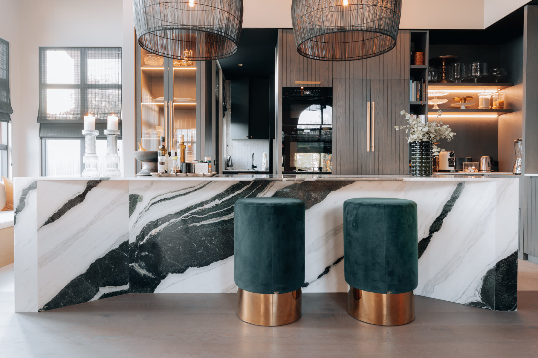 The Bird House — a marble island with green velvet stools under tall windows.
